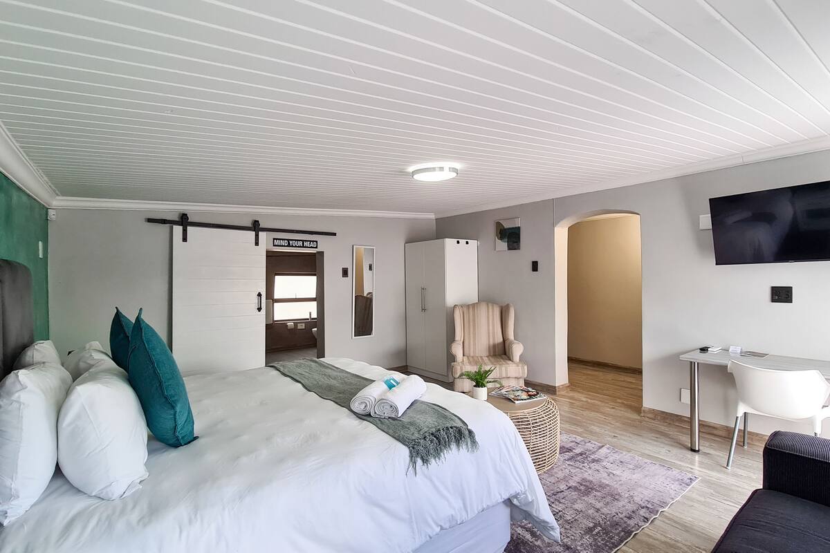 A modern bedroom with a bed, a desk, a chair, a TV, and a wardrobe.