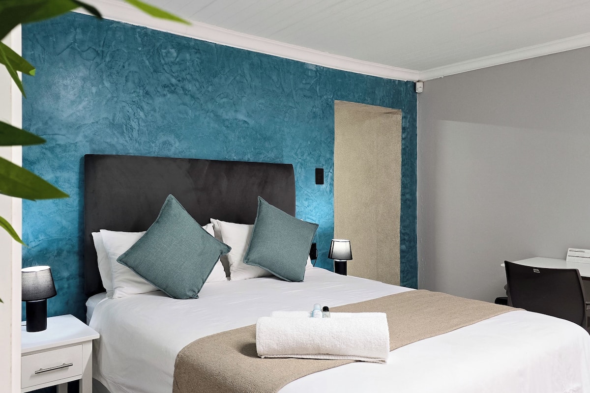 A modern hotel room with a large bed, two bedside tables, a desk, and a chair.