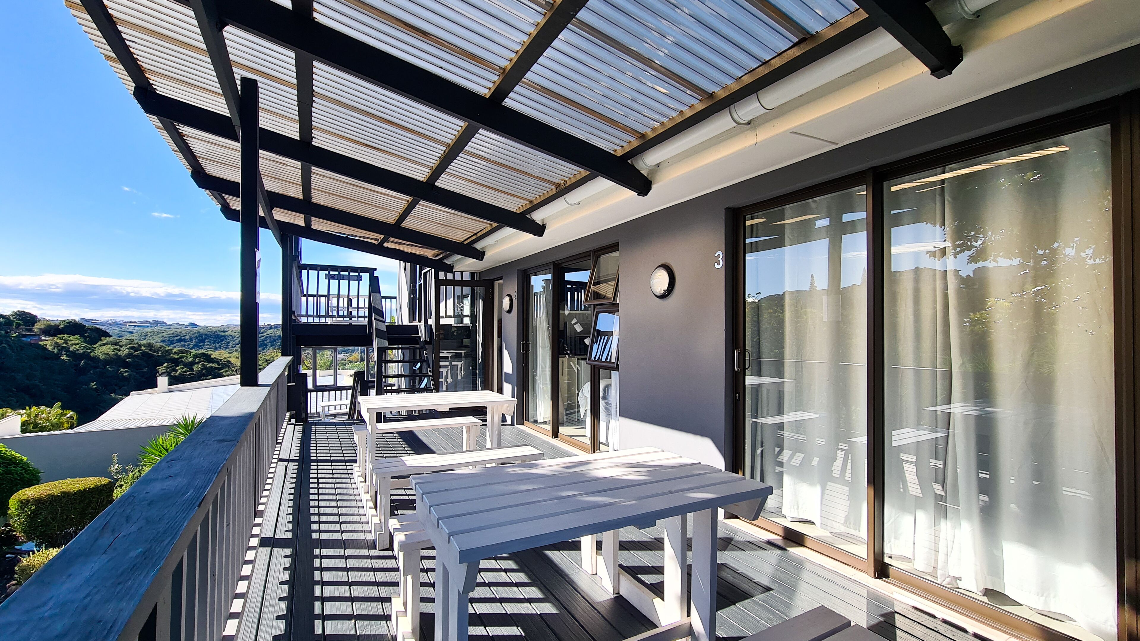 Un balcón con puerta de cristal, terraza de madera y mobiliario exterior.