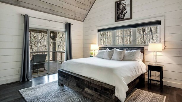 Una camera da letto con un letto grande, una testiera in legno, una finestra con vista sugli alberi e una porta che dà su un balcone.