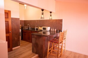 A kitchen with a central island, wooden cabinets, a microwave, and a bar stool. - Belle Etoile - Cinnamon Studio Suite (Soufriere)
