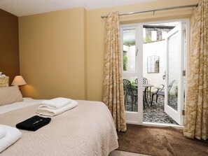 A hotel room with a bed, a lamp, a window with curtains, and a view of an outdoor patio with chairs and a table. - Jenny's (Ambleside)