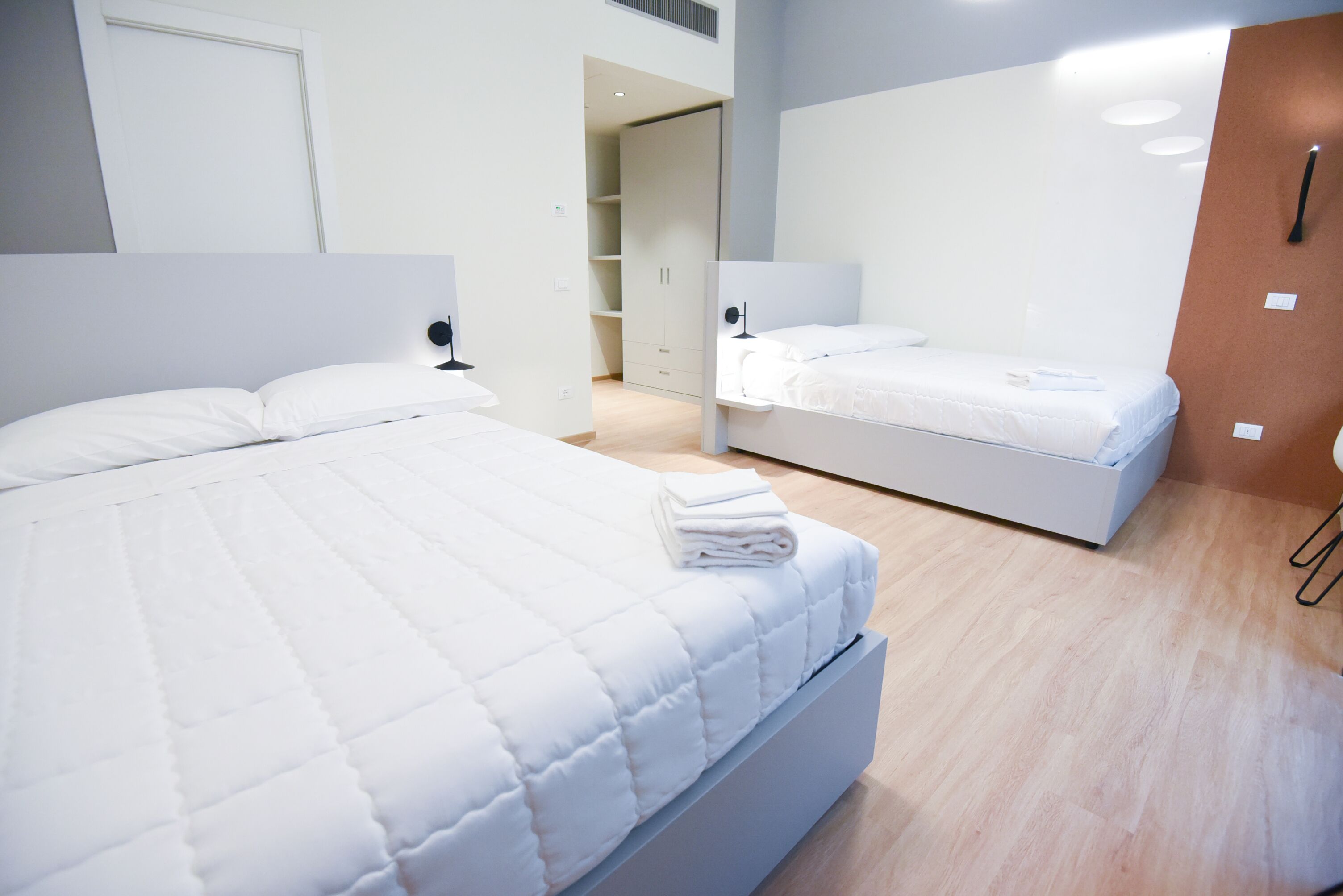 A modern bedroom with a large bed, a smaller bed, and a walk-in closet.