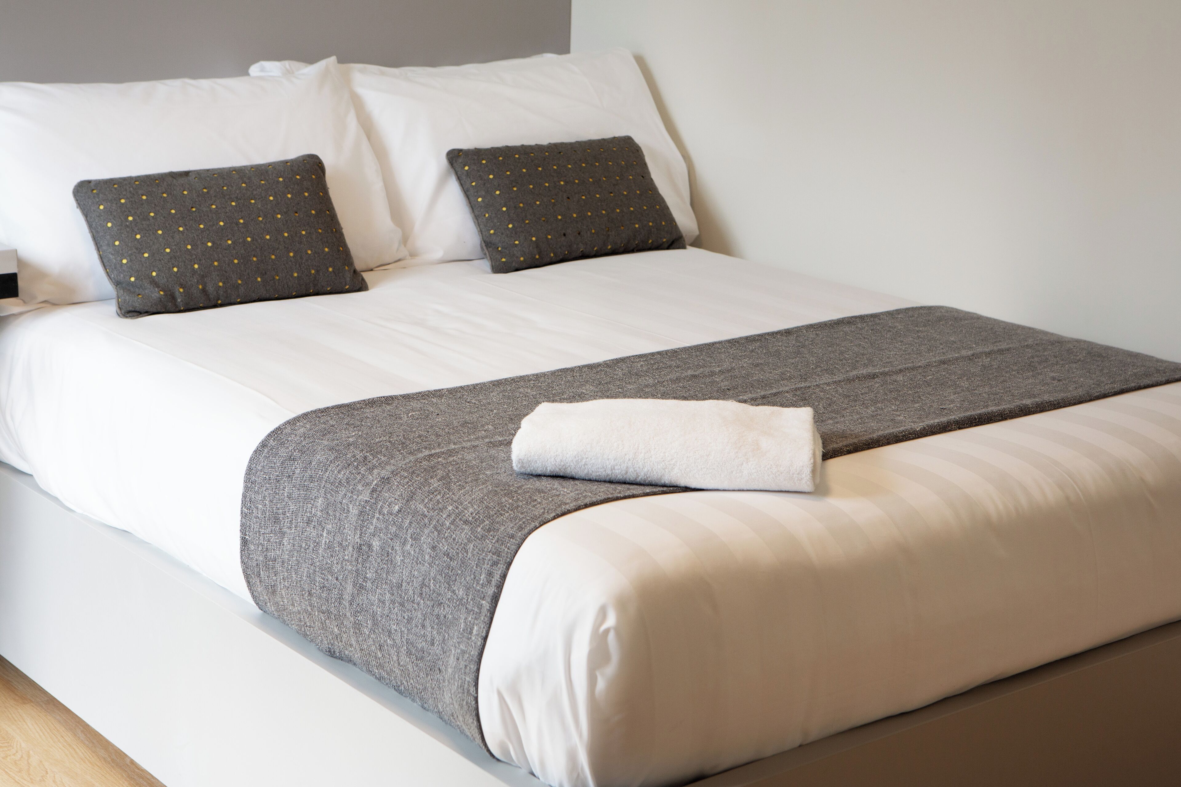 A neatly made bed with white linens, two grey pillows with gold dots, and a grey blanket.