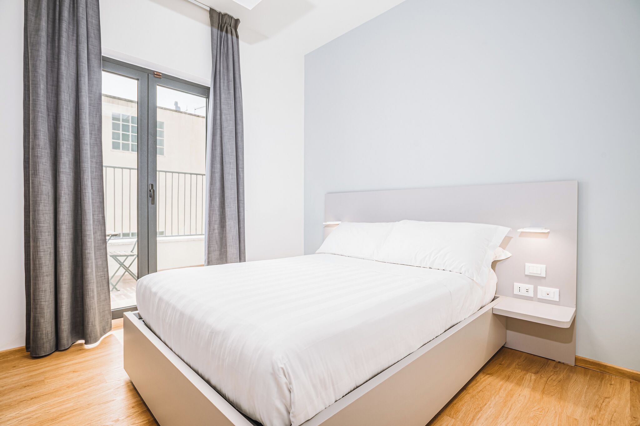 Une chambre moderne avec un grand lit, une table de chevet et une vue sur un balcon.
