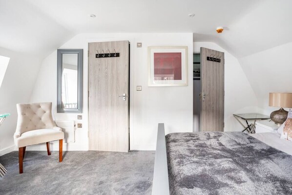 A bedroom with a bed, a chair, a desk, and two wardrobes.