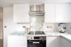 Eine moderne Küche mit weißen Schränken, einer Edelstahl-Dunstabzugshaube, einem eingebauten Backofen und einer Marmorarbeitsplatte.