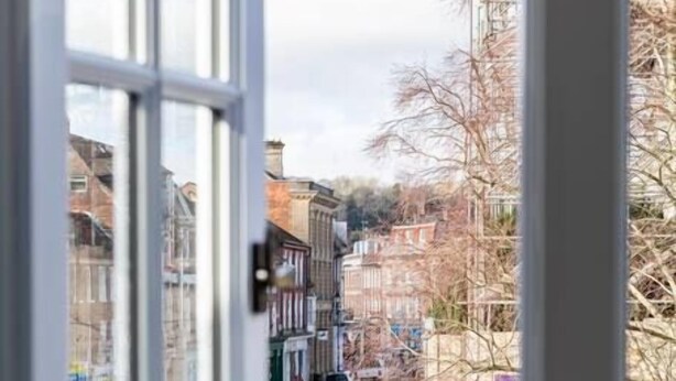 A view through a window of a street with buildings, a road, and a grassy area. - The Secret: Stylish and Spacious En Suite Bathroom (Blandford Forum)