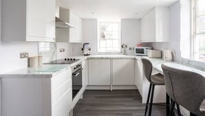 A modern kitchen with white cabinetry, a marble countertop, and a window providing natural light. - The Secret: Stylish and Spacious En Suite Bathroom (Blandford Forum)