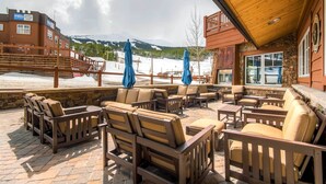 Un espace extérieur aménagé avec plusieurs chaises et tables, un mur en pierre et une vue sur un paysage montagneux enneigé.