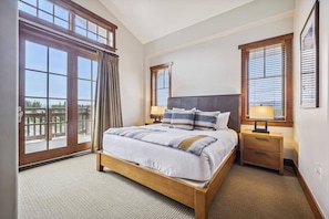 Un dormitorio con una cama grande, dos mesitas de noche, una ventana con persianas y vistas al exterior.