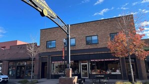 A two-story building with a storefront, a street sign above, and a tree with autumn leaves. - Arch Building Lofts - Unit 6 (Redmond)