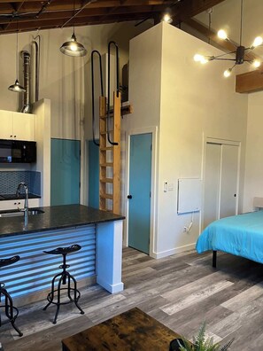 A compact kitchen with a central island, bar stools, and a wooden ladder. - Arch Building Lofts - Unit 6 (Redmond)