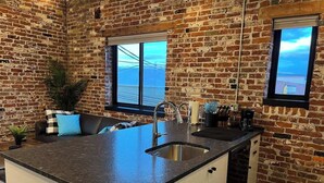 A kitchen with a large island, a sink, and a window overlooking a scenic view. - Arch Building Lofts - Unit 6 (Redmond)