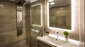 A modern bathroom with a glass shower enclosure, a large mirror, and a vanity with a sink and a small potted plant. - Malia Palace by Luxury Living Apartments (Hersonissos)