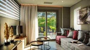 A modern living room with a sofa, a TV, a small table, and a balcony with a chair and table. - Malia Palace by Luxury Living Apartments (Hersonissos)
