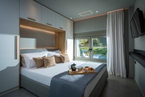 A modern bedroom with a large bed, a bedside table with a tray of breakfast, and a TV mounted on the wall. - Malia Palace by Luxury Living Apartments (Hersonissos)