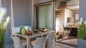 Un espace repas moderne avec une table en verre, des chaises en osier et une vue sur la cuisine grâce à une porte vitrée.