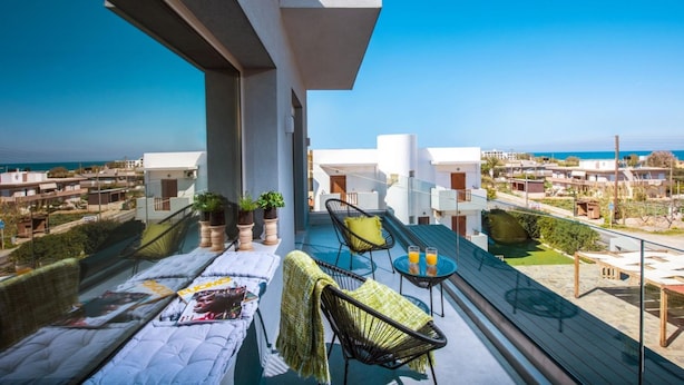 Un balcon avec vue sur la mer, aménagé avec des chaises et une table, et agrémenté de plantes en pot.