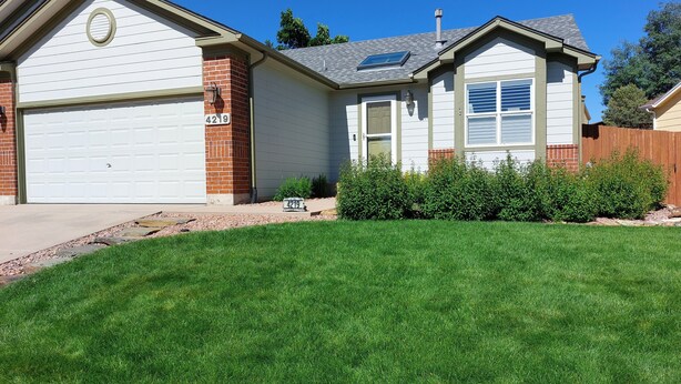 A single-story house with a garage, a brick chimney, and a well-maintained lawn. - Spacious family suburban home (Colorado Springs)