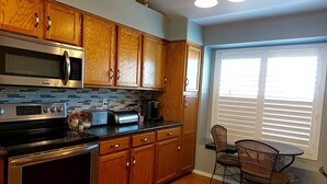 A kitchen with wooden cabinets, a microwave, a toaster, and a dining area with a chair. - Spacious family suburban home (Colorado Springs)