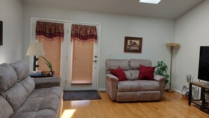 A living room with a grey sofa, a beige armchair with red cushions, a floor lamp, and a TV on the right. - Spacious family suburban home (Colorado Springs)