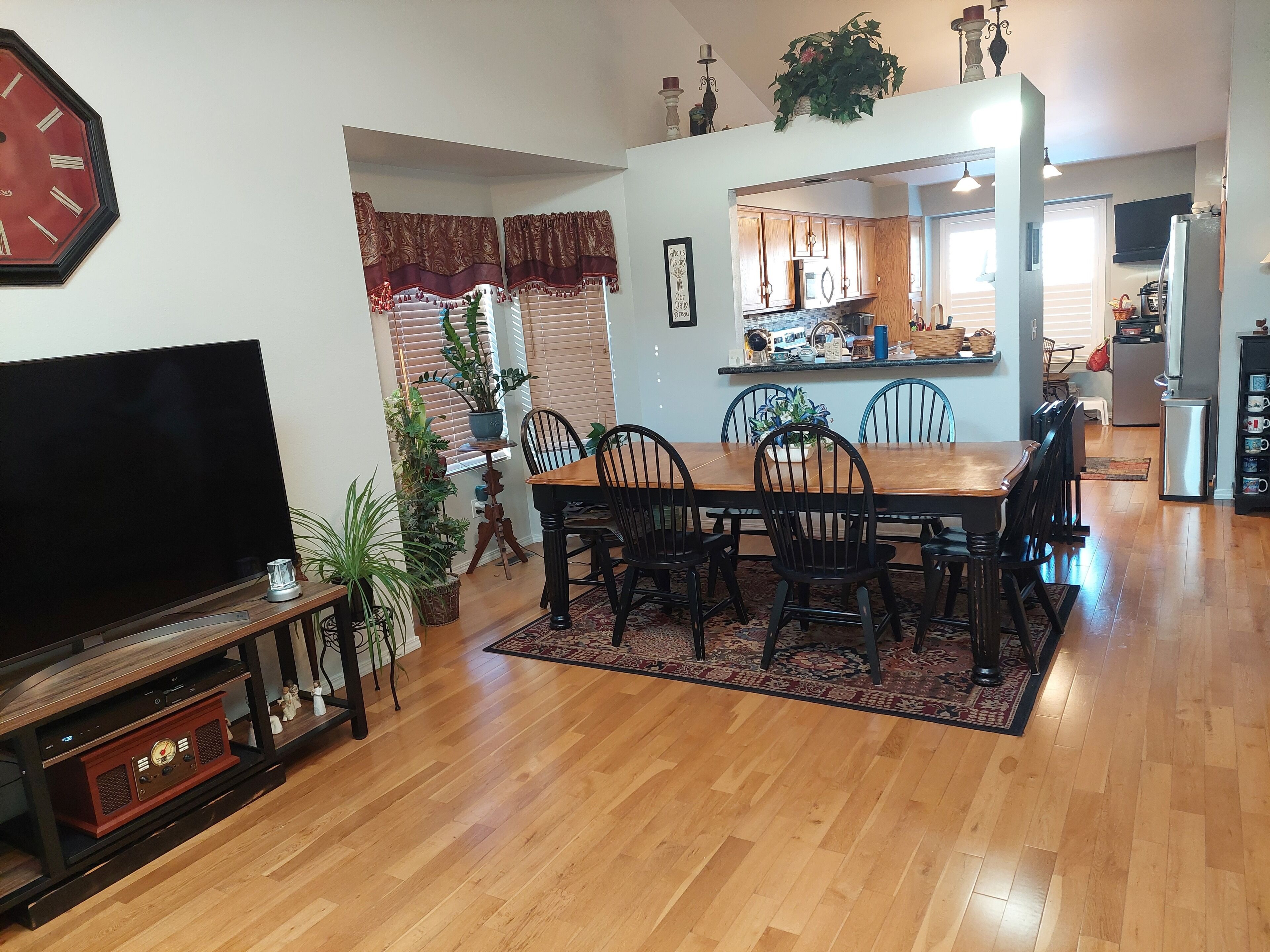 A dining area with a wooden table and chairs, a television, and a clock on the wall.