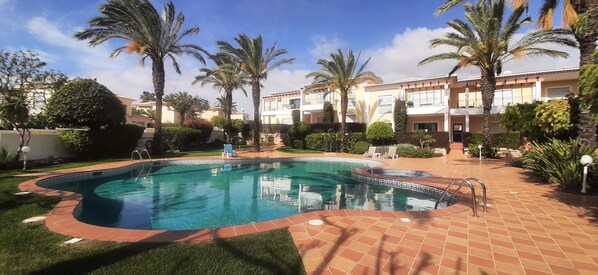 A swimming pool surrounded by palm trees and a building with balconies. - Apartment Buganvilia Porto de Mós (Lagos)