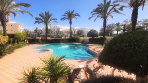 A swimming pool surrounded by palm trees and a brick pathway. - Apartment Buganvilia Porto de Mós (Lagos)