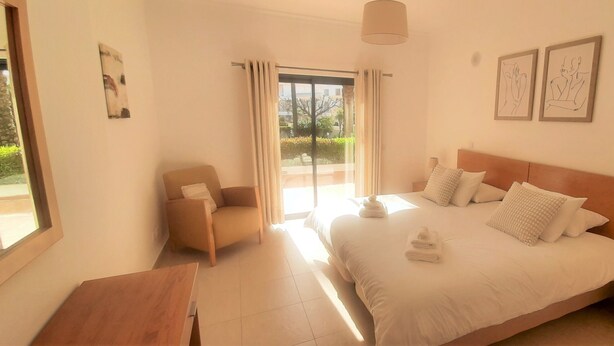 A bedroom with a bed, a chair, a nightstand, and a window. - Apartment Buganvilia Porto de Mós (Lagos)