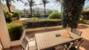 A wooden table with chairs, a small pool, and surrounding greenery. - Apartment Buganvilia Porto de Mós (Lagos)