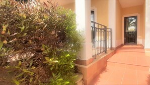 A covered walkway leading to a building entrance with a metal gate, surrounded by greenery. - Apartment Buganvilia Porto de Mós (Lagos)