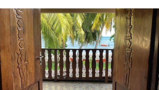 A wooden door with intricate carvings, leading to a balcony with a view of palm trees and the sea. - Villa Carla - Grandiose stays by the sea (Antsiranana)