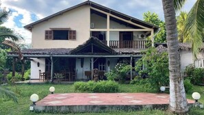 A two-story house with a balcony, surrounded by lush greenery and palm trees. - Villa Carla - Grandiose stays by the sea (Antsiranana)