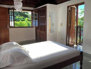A bedroom with a bed, wooden walls, and a view of greenery outside.