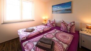 A bedroom with two beds, a window, a nightstand with a lamp, and a painting on the wall.