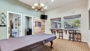 A room with a billiards table, a bar area with stools, a television, and a window with a view.