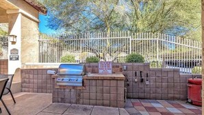 An outdoor grill area with a stone wall, a metal grill, and a trash can.