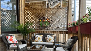 Une terrasse en bois avec des meubles en osier, une table basse en verre et un panneau d’accueil.