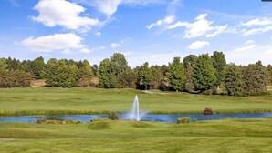 Un campo de golf con un estanque y una fuente, rodeado de árboles.