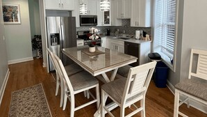 Une cuisine moderne avec des meubles blancs, un réfrigérateur en acier inoxydable, un four à micro-ondes et un coin repas comprenant une table en verre et des chaises blanches.
