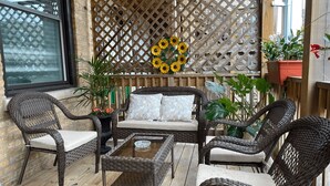 Un espace de détente extérieur aménagé avec des meubles en osier, une table basse avec un plateau en verre, des fauteuils rembourrés et un plancher en bois.
