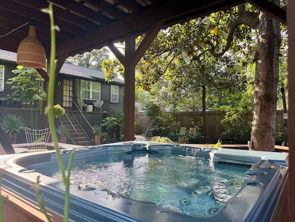A hot tub under a wooden pergola with a house in the background.