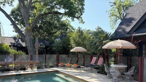 A swimming pool with lounge chairs and umbrellas, surrounded by trees and a fence.