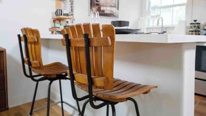 A kitchen with two wooden chairs with black metal frames, a white countertop, and a window with natural light.
