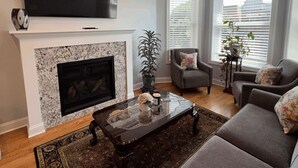 A living room with a fireplace, a flat-screen TV mounted above it, and a sofa set. - Wrigleyville Inn - Unit 3 (Chicago)
