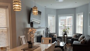 A modern living room with a wooden dining table, two chairs, a sofa, and a coffee table. There are two pendant lights hanging from the ceiling. - Wrigleyville Inn - Unit 3 (Chicago)