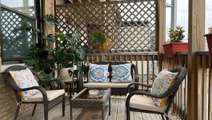 A wooden deck with wicker furniture, including chairs and a table, surrounded by potted plants and a lattice fence. - Wrigleyville Inn - Unit 3 (Chicago)