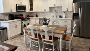 Une cuisine moderne avec des meubles blancs, des appareils en acier inoxydable et une table à manger en bois, accompagnée de chaises.