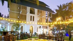 An outdoor dining area with tables and chairs, a building in the background, and string lights. - Hotel Leaf on Lagoon (Seeduwa - Katunayake)